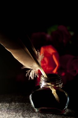 Inkwell with feather against black background,lowkey with red roses clipart