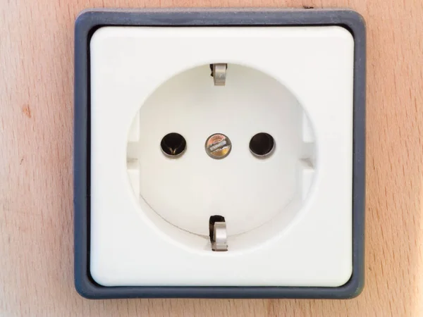 frontal detail view of a single white socket with grey frame on wooden background