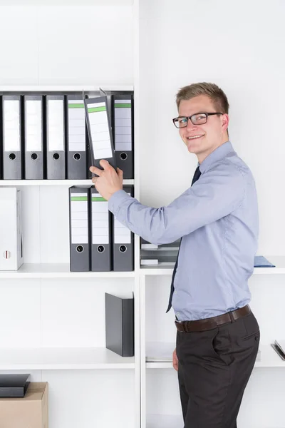 Young Businessman Glasses Stands Front Shelf Office Pulls File Order — Stock Photo, Image