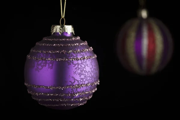 手前は紫のクリスマスボール縦に縞模様のクリスマスボール黒の前のサイドライトのファジィの背景 — ストック写真