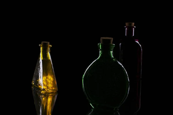 Три Цветные Декоративные Бутылки Стеклянной Пластине Черном Фоне — стоковое фото