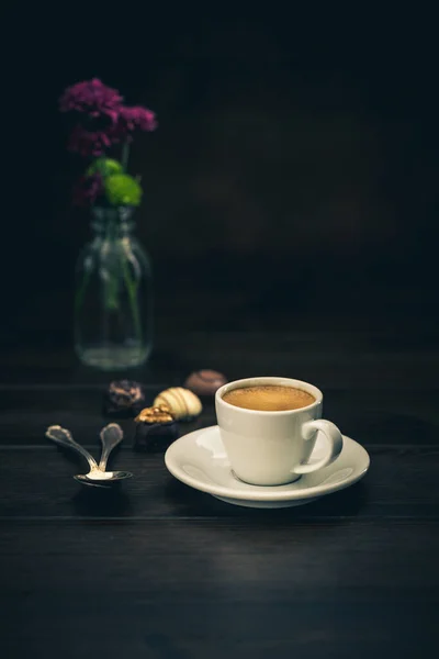 Espresso with chocolates with flowers on a wooden background