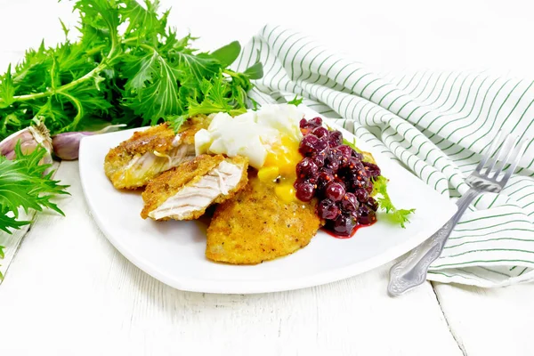 Fried turkey breast in breadcrumbs with cranberry sauce, boiled egg, baked parsnip and lettuce in a plate, towel and fork on light wooden board background