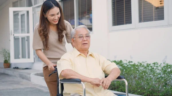 stock image Disabled senior man on wheelchair with daughter, Happy Asian generation family having fun together outdoors backyard, Care helper young woman walking an elderly man smiling and laughed