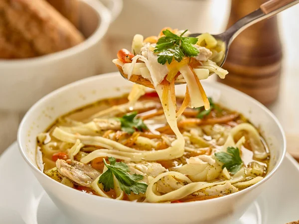 Noodle soup. Delicious soup with noodle, pieces of chicken and vegetables in white bowl served with spices and breads on light wooden background.