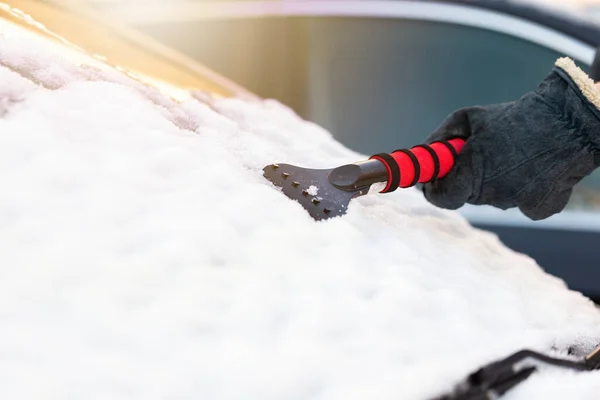 人们在冬天用刮胡刀从汽车的挡风玻璃上刮雪 戴手套的人的手在阳光下从宽面罩上擦去白色的盖子 早上清除车辆上的霜冻 — 图库照片