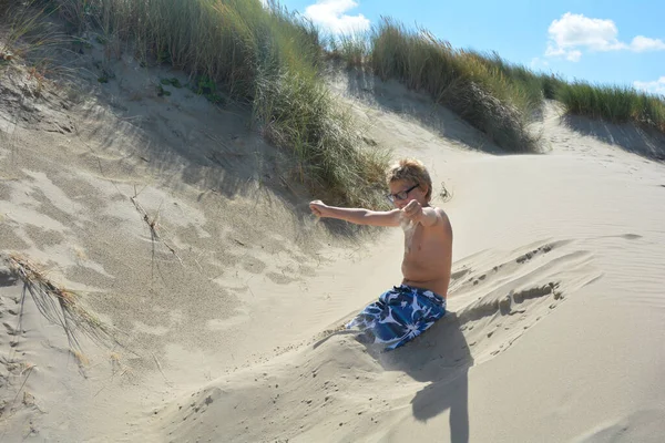 언덕에 소년은 헤엄치는 줄기로 모래를 손으로 퍼내고 — 스톡 사진