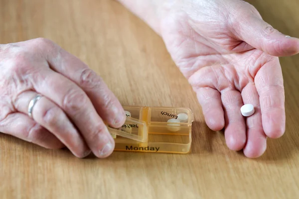 一位年长的老妇人在木桌 健康概念上的药盒里 用自己的双手给自己药物治疗了一个星期 — 图库照片