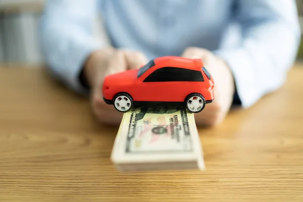汽车保险的概念 持有木制背景的玩具钱和美元钞票的人 — 图库照片