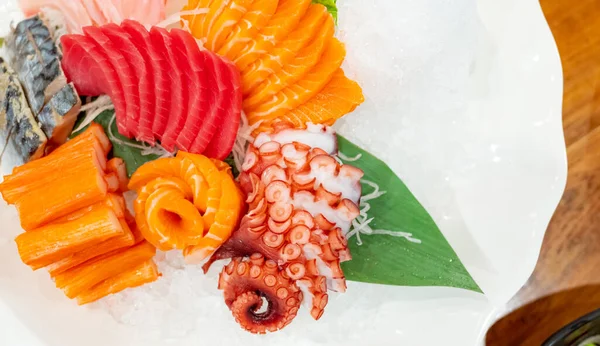 Japanese food combo set. Salmon, tuna sashimi, giant octopus and Crab sticks serve with crushed ice in white plate on restaurant table. Fish meat sliced. Seafood buffet. Healthy Japanese food.
