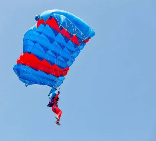 青い空にパラシュートの天蓋の下で降下する赤いスーツのパラシューパー — ストック写真
