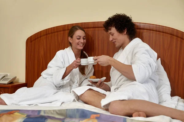 バスローブを着たカップルがベッドに座ってコーヒーを飲み — ストック写真