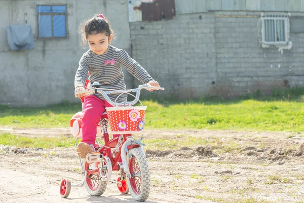 小女孩骑着一辆红色四轮自行车在室外土路上 — 图库照片