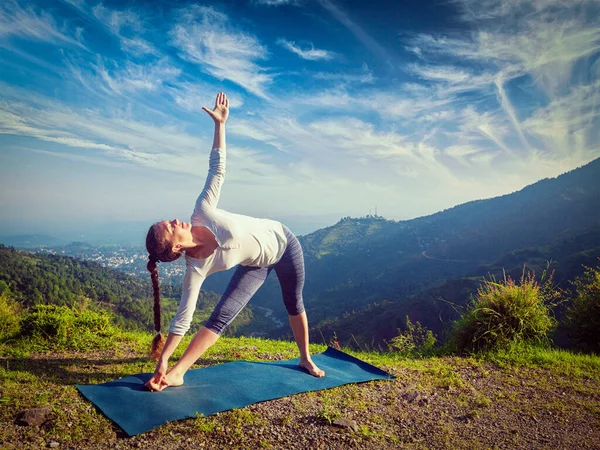 做Ashtanga Vinyasa Yoga Asana Utthita Trikonasana 伸展三角形的女人早上在山上摆姿势 复古效果过滤嬉皮士风格的图像 — 图库照片
