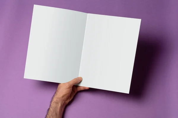 紫色の背景に空白のページを持つ開いた三つ折りのカタログを保持する男性の手 あなたのデザインのためのモックアップシリーズテンプレート ページ選択パスが含まれています — ストック写真