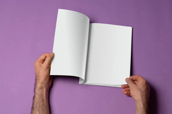 紫色の背景に空白のページを持つ開かれたブックカタログを保持する男性の手 あなたのデザインのために準備ができてモックアップシリーズテンプレート ページ選択パスが含まれています — ストック写真