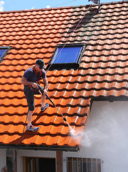 Workers cleaning the roof of moss and dirt with a high pressure cleaner. Secured with a safety rope.