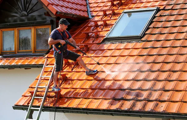 Workers cleaning the roof of moss and dirt with a high pressure cleaner. Secured with a safety rope.