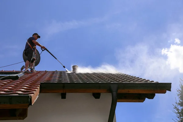 Workers cleaning the roof of moss and dirt with a high pressure cleaner. Secured with a safety rope.