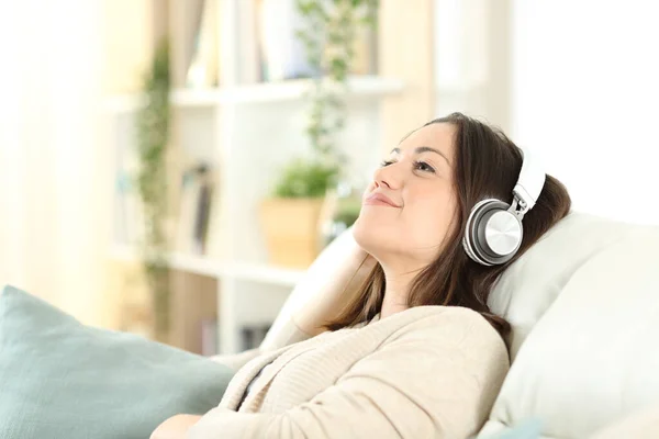 满意的女人放松地坐在沙发上听家里的音乐 — 图库照片