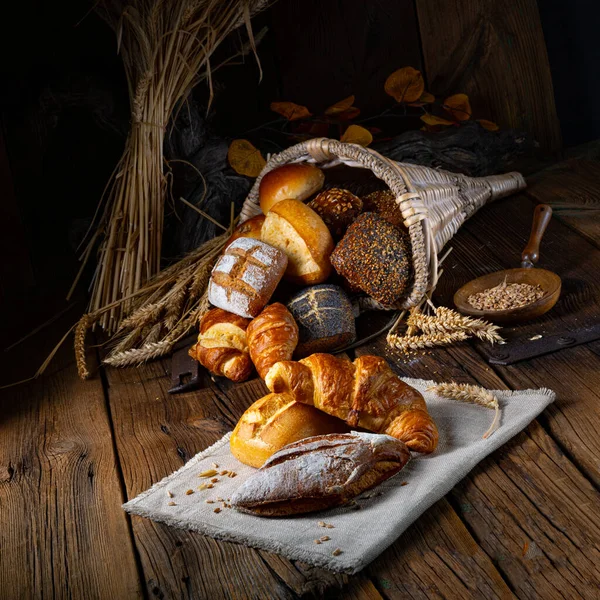 焼きたてのパンに小麦とさまざまな種類のライ麦の新鮮な耳が木のテーブルの上に — ストック写真