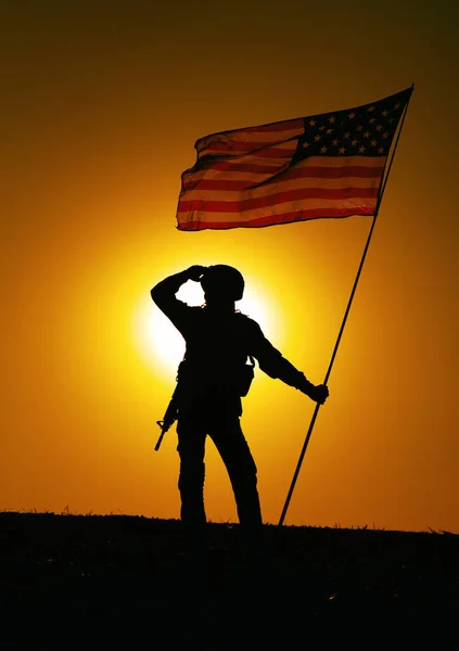 米軍兵士のシルエット 海兵隊の戦闘機やヘルメットの特殊部隊のライフルマン 風の国旗に手を振って丘の上に立つ武装ライフル 遠くの夕日の空を背景に見て — ストック写真