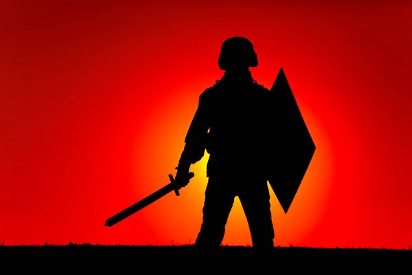 戦闘ヘルメット 武装剣と盾の現代の兵士のシルエットは 地平線の後ろに夕日の空と太陽の設定の背景に立っている 軍国主義 国家防衛 愛国主義の概念 — ストック写真