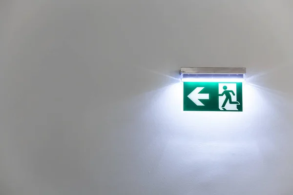 green illuminated emergency exit sign on a white wall of a building.