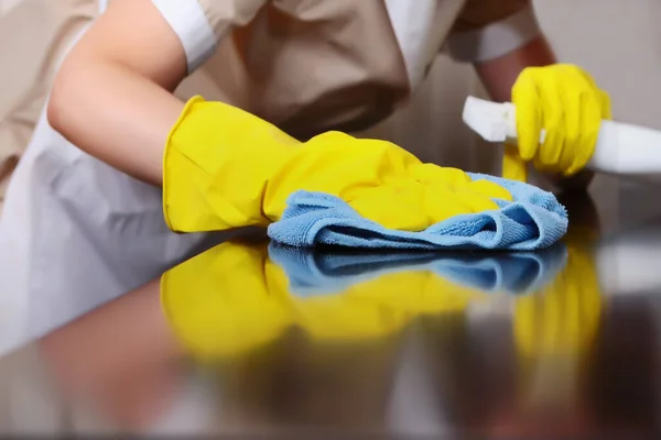 A uniformed maid is dusting the furniture. Cleaning in the hotel room. The person is unrecognizable. Out of focus. The concept of hotel business and cleaning. High-quality service in the hotel. Hands in protective gloves. Copy space.