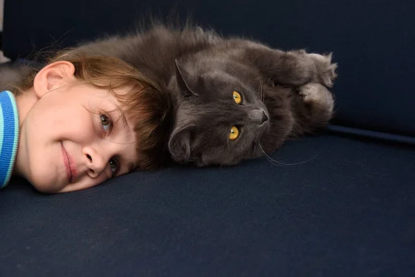 女の子は彼女の頭を猫に押し当てソファの上に横たわる — ストック写真