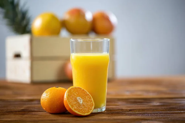 木製のテーブルの上に立つオレンジジュースのデューイグラス 透明なカップの甘い飲み物のフルーツの半分の横にカットされます 新鮮な健康的な液体 — ストック写真