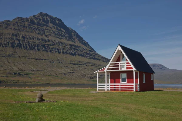 東アイスランドのエスキフィヨルドゥールを背景にした強力なホルマティドゥール山のある伝統的な赤塗りの木製パネルハウス ストックフォト
