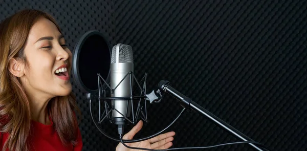 Musician producing music in professional recording studio. Young asian woman in red t-shirt singing in front of black soundproof wall. (Close up)