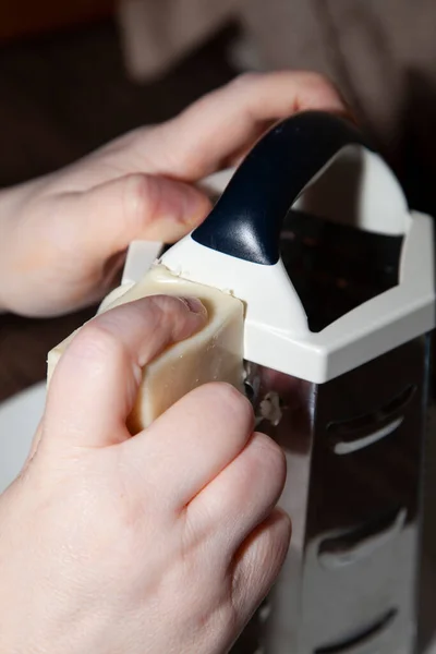 女人用一个大的金属奶酪研磨机在白盘上切碎白奶酪 — 图库照片