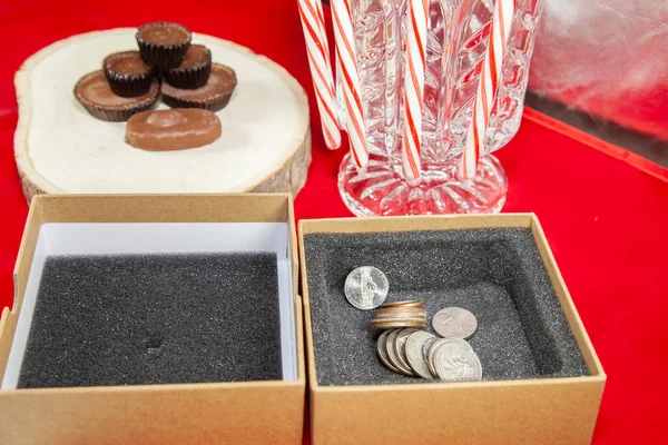 Pennies, nickels, dimes, quarters, and dollar coins in a gift box next to candy canes and Christmas chocolates