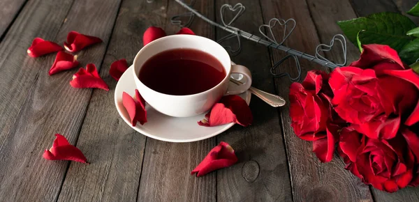 濃いヴィンテージの板の上に赤いバラと心を持つお茶のカップ バレンタインデーのコンセプトの朝食の背景 — ストック写真
