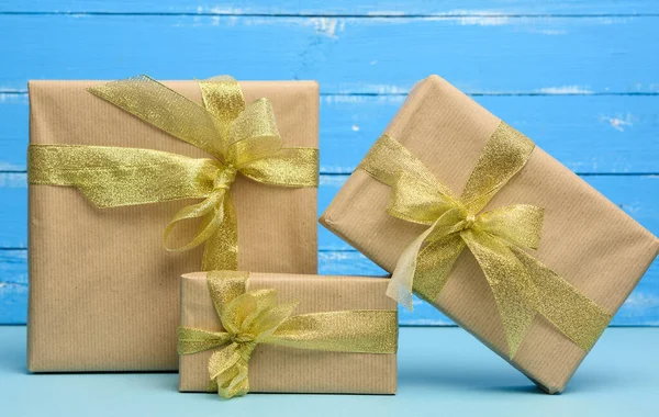 用褐色牛皮纸包裹的一堆堆礼物 用金色缎带捆扎 蓝色背景的盒子 — 图库照片