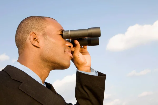 young businessman looking through binoculars on a background of sky