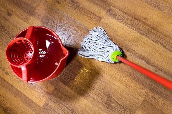 top view of rope mop cleans wooden laminate floor near bucket with water at home