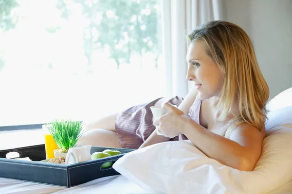 若い女性とお茶を飲み読書本をベッドの上で — ストック写真