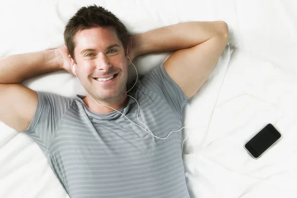 年轻人在床上用耳机听音乐 — 图库照片