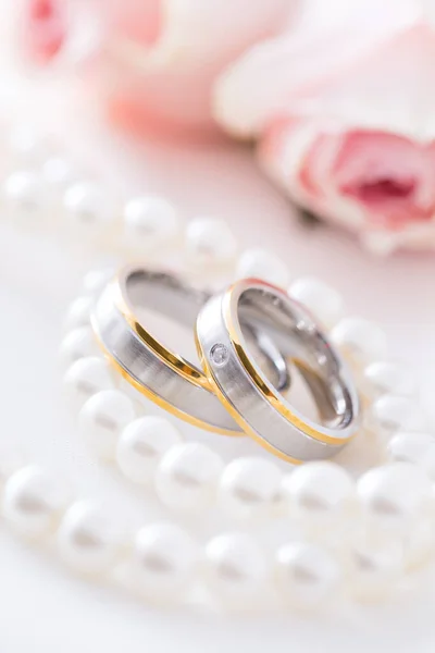 现代婚戒以珍珠项链为背景 粉红的玫瑰 柔和的焦点 — 图库照片