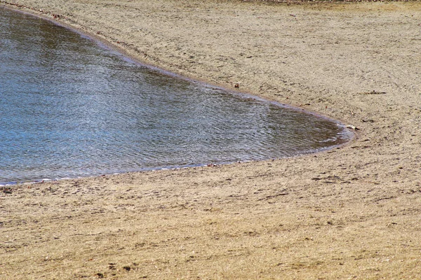 美しい湖の海岸線が緩やかにカーブする 水は茶色の砂浜に対する小さな波と波紋で落ち着いています 選択的フォーカスとコピースペースと美しい自然背景 — ストック写真