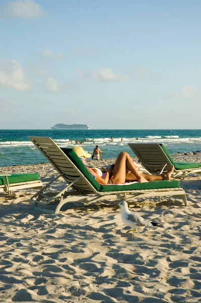 Side profile of a woman reclining on a lounge chair on the beach