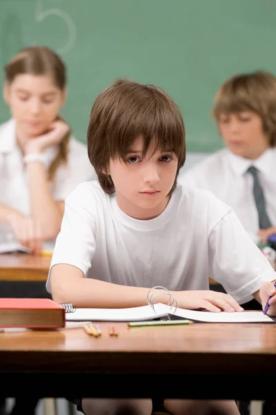 一个坐在桌旁在教室里学习的小男孩的画像 — 图库照片