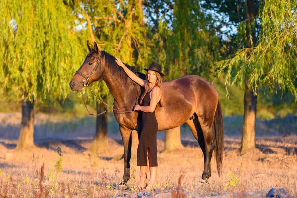 一个女孩把马抱在树后 夕阳西下的光芒落在了他们身上 — 图库照片
