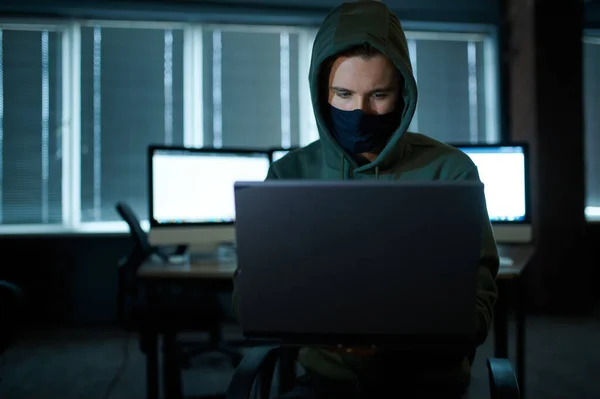 头罩里的男性网络黑客拿着笔记本电脑 前视镜 非法网络程序员在工作场所 犯罪职业 数据黑客攻击 网络安全 — 图库照片