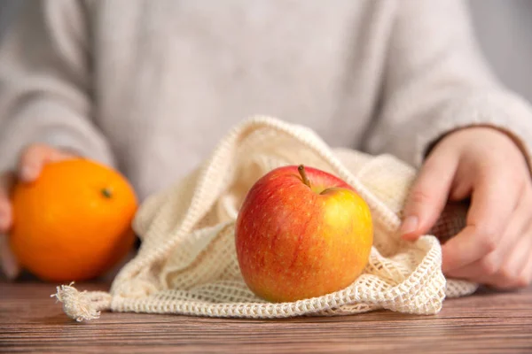 新鮮な果物 リンゴとオレンジ 木製のテーブルの上に環境に優しいネットバッグを持つ女性の手を閉じる — ストック写真