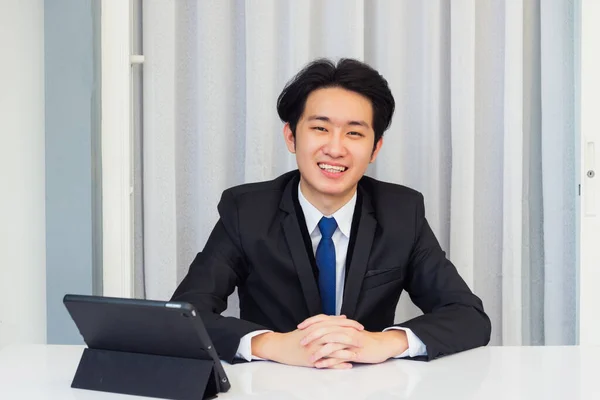 自宅から仕事 アジアの若いビジネスマンのビデオ会議コールやFacetime彼は自宅のオフィスでスマートデジタルタブレットコンピュータを使用して机の上に手で座ってカメラを見て笑顔 — ストック写真