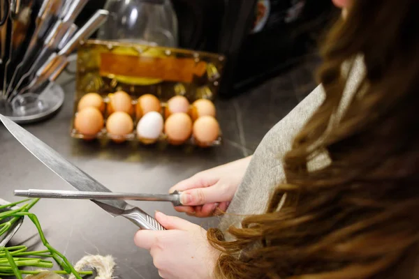 Woman sharpening kitchen knife with grindstone in the kitchen, kitchen knife. Close up view on hands.